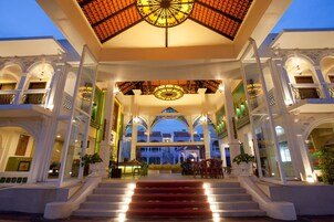 Un amplio vestíbulo de hotel con una escalera central, techo ornamentado y varios balcones.