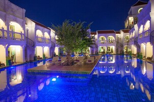 Zona de piscina con un árbol en el centro, rodeada de edificios blancos con balcones y escaleras.
