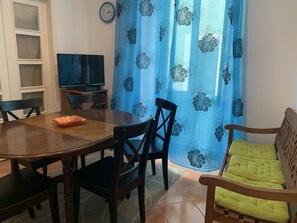 A dining area with a wooden table, chairs, a television on a stand, and a blue floral curtain. - House and Rooms in Lisbon (Lisbon)