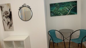 Comedor con una mesa blanca y dos sillas color turquesa, un espejo redondo y dos cuadros colgados en la pared.