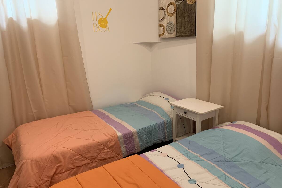 A bedroom with two beds, a small white table, and a wall decoration.