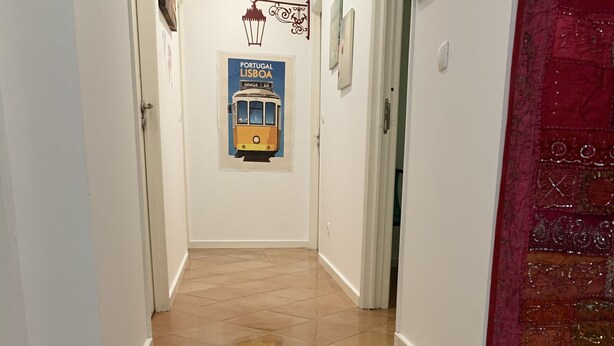 Una escalera con baldosas color crema que conduce a una habitación con una puerta roja y una lámpara fijada a la pared.