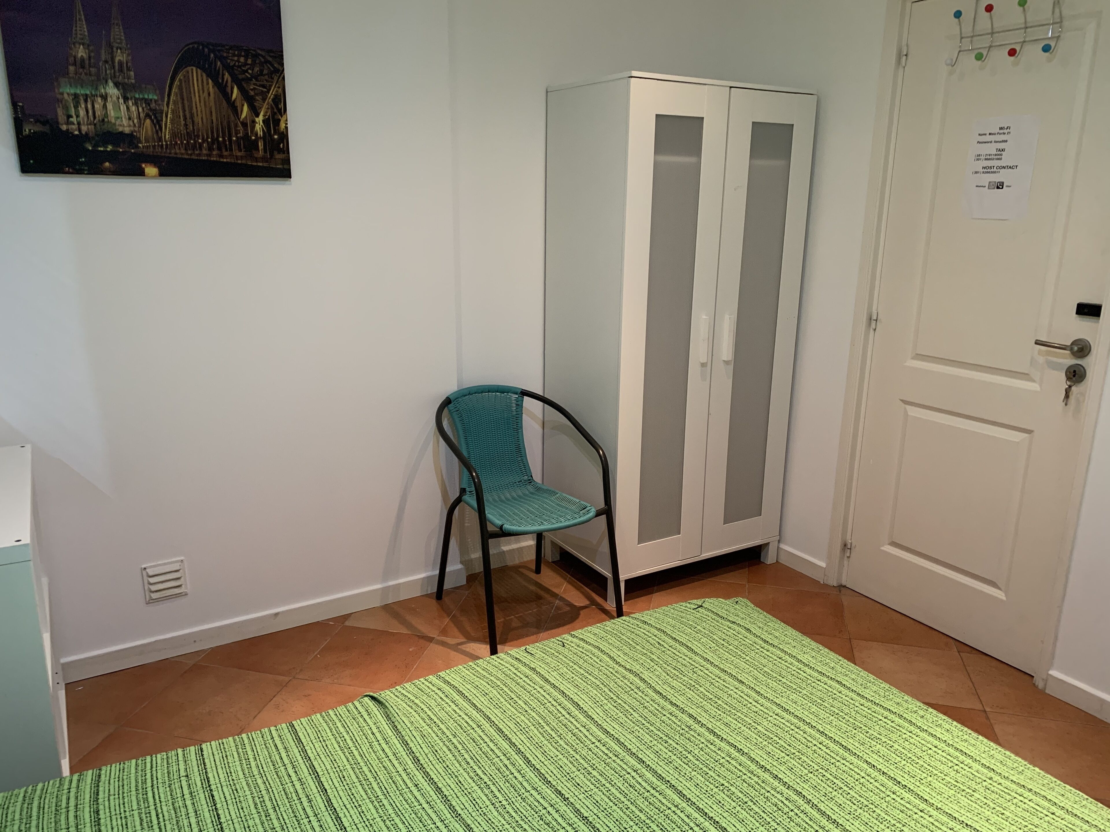 A room with a teal chair, a white wardrobe, and a green rug.