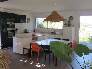 A modern kitchen with white cabinetry, a dining area with a large table and chairs, and a view of greenery outside.