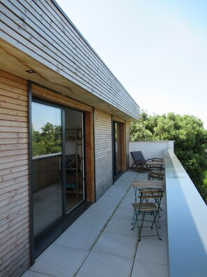 Un bâtiment moderne doté d’un toit en pente, de grandes fenêtres et d’un balcon aménagé avec du mobilier d’extérieur.