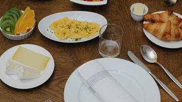 A breakfast setting with various dishes including croissants, fruit, and cheese.