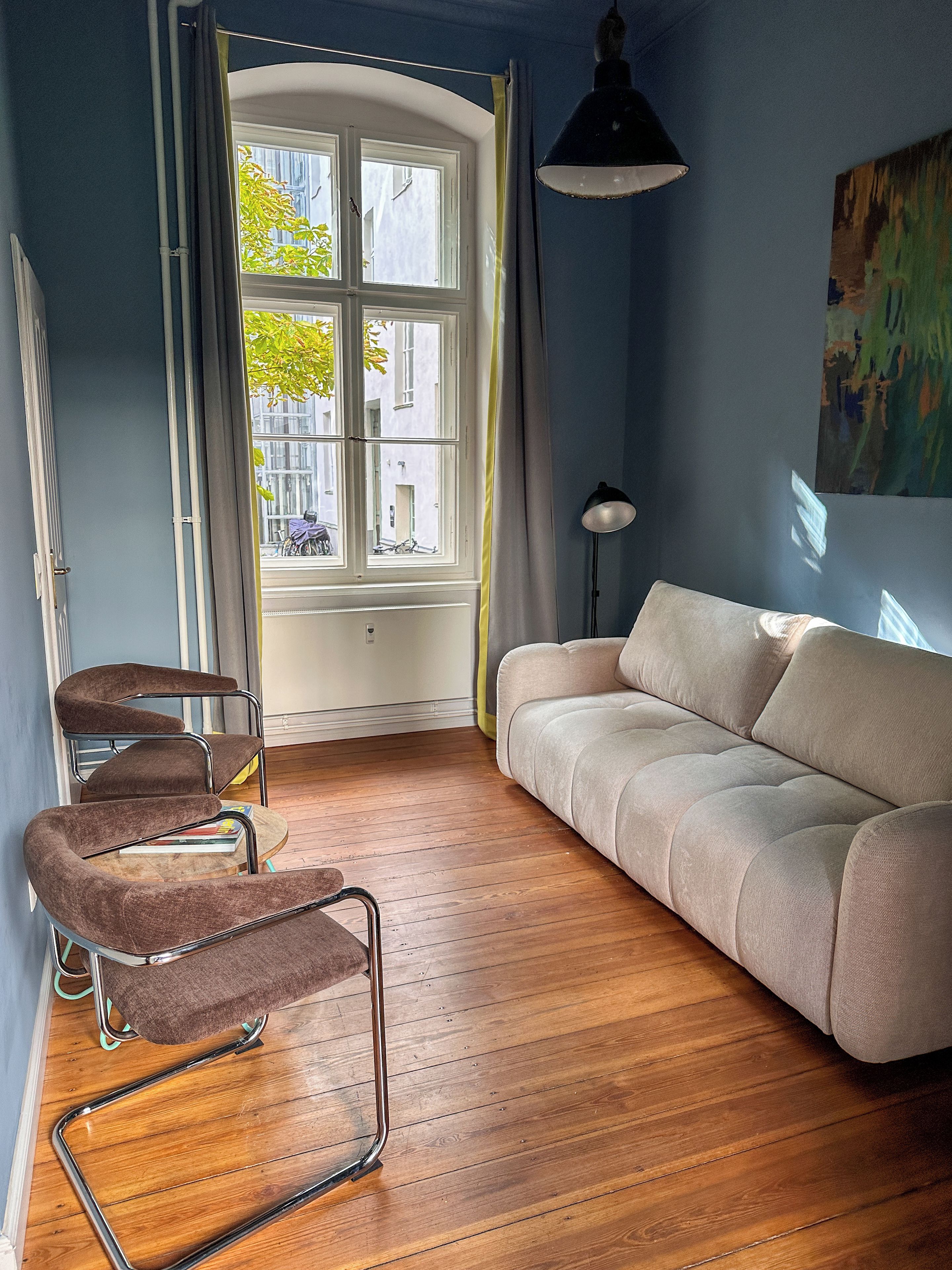 Ein Zimmer mit einer Couch, einem Sessel, einer Lampe und einem Fenster mit Vorhängen.