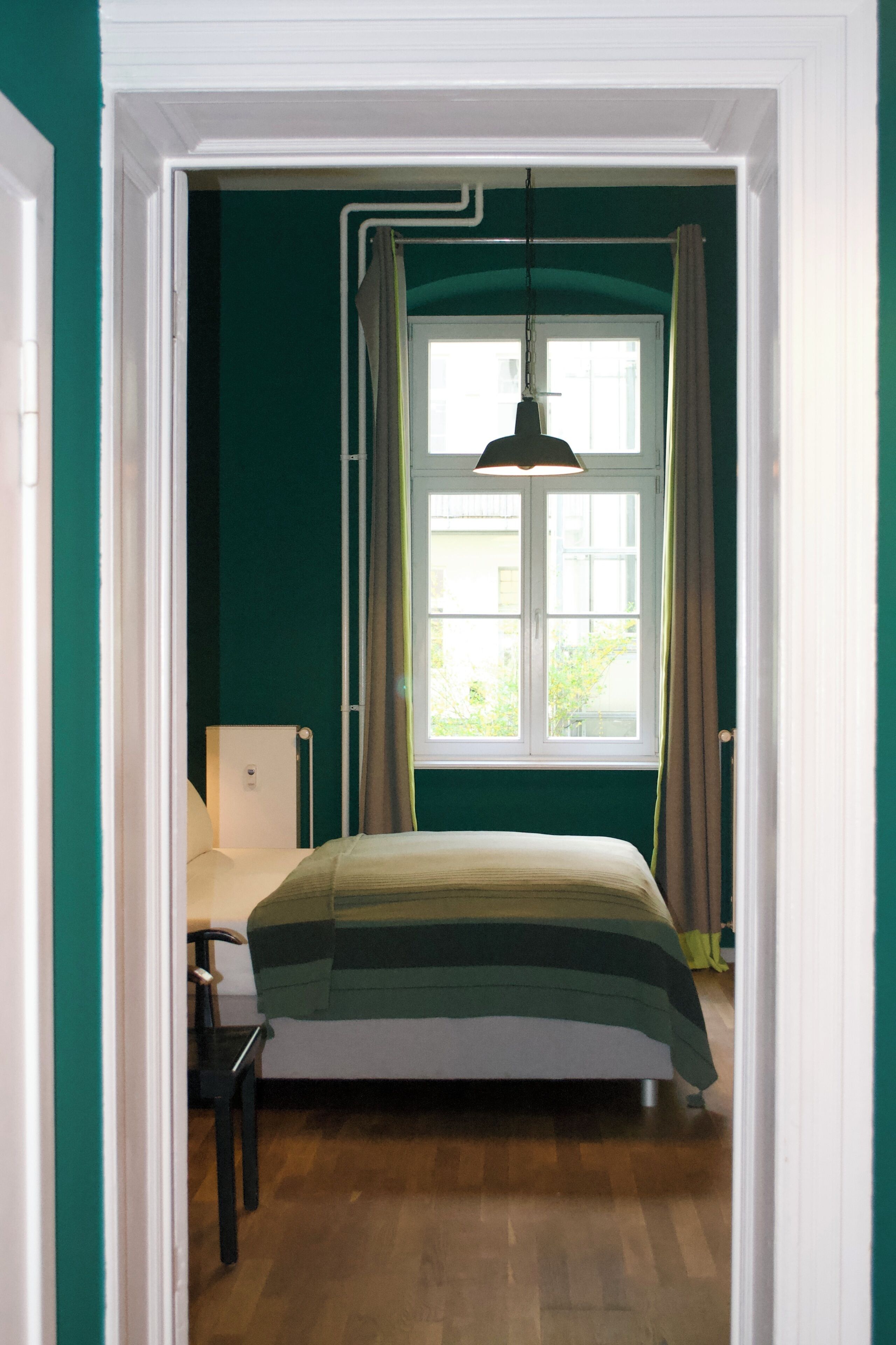 Une chambre à coucher avec un lit, une chaise, une fenêtre avec des rideaux et un luminaire suspendu.