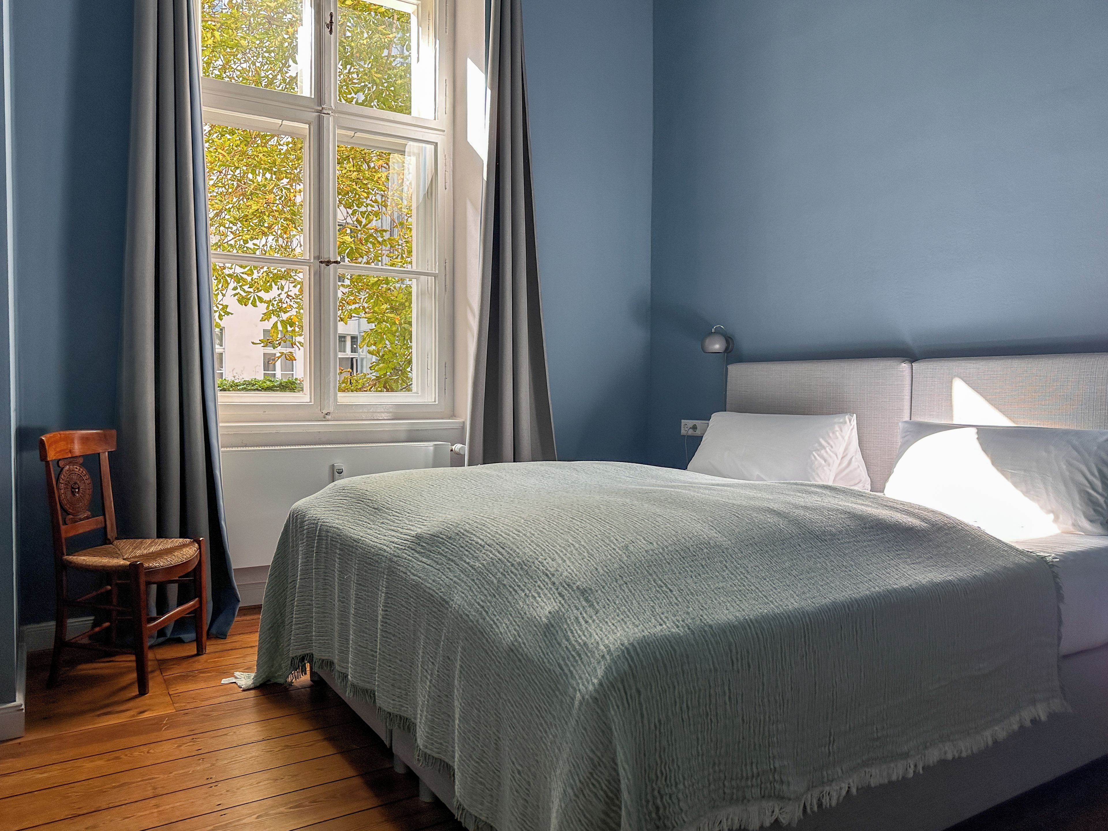 Ein Schlafzimmer mit Bett, Sessel, Fenster und Lampe.