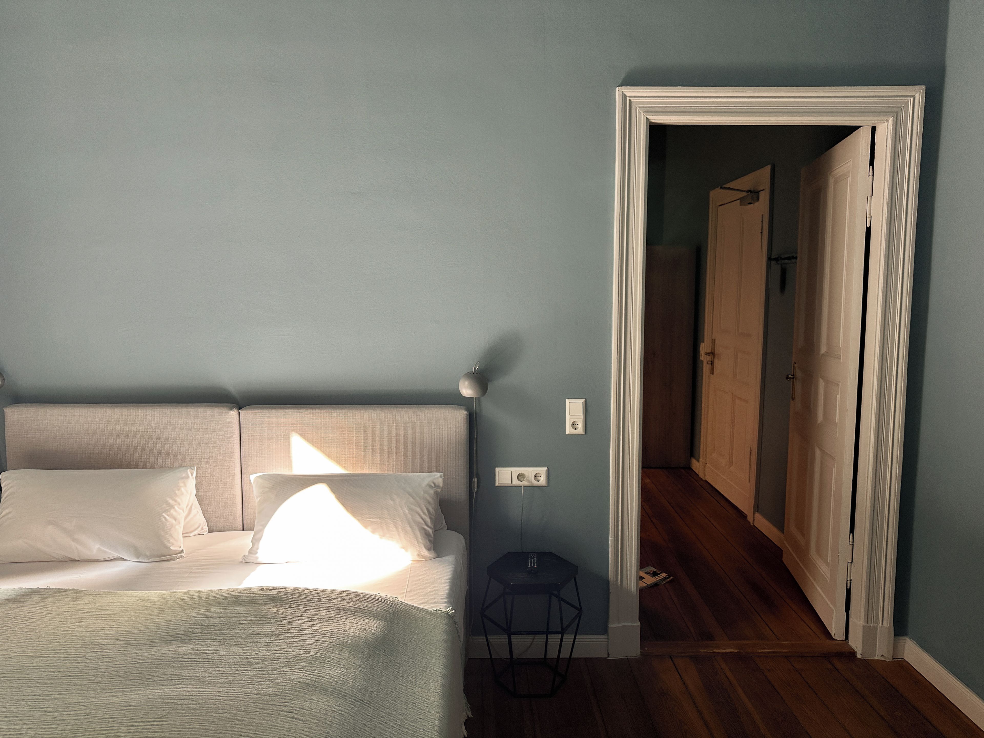 Quarto com cama, abajur e um banquinho.