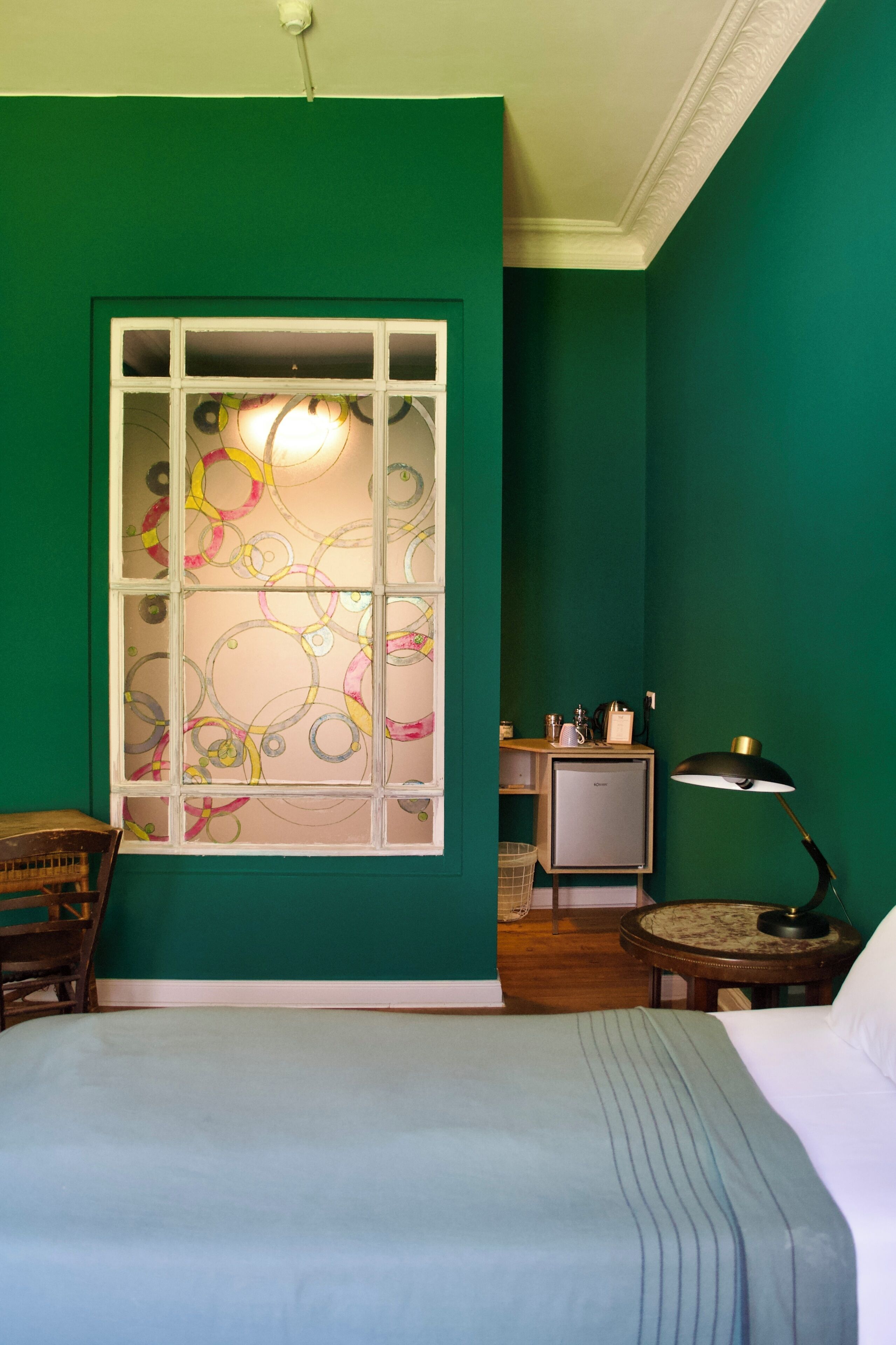 Una habitación con cama, escritorio, silla, lámpara y ventana con diseño decorativo.