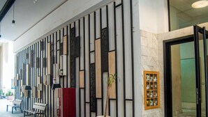 Un área de recepción moderna con un diseño de panel vertical, una planta en maceta grande, un banco y una exhibición de objetos en la pared.