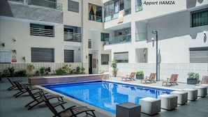 Un moderno edificio de apartamentos con piscina, mobiliario exterior y un cartel que indica zona para no fumadores.