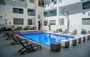 A modern apartment building with a swimming pool, outdoor seating, and a sign indicating a no-smoking area. - Studio les pieds dans l'eau (Mohammédia)