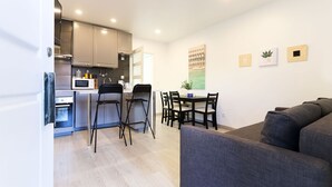 A modern kitchen with a microwave, stove, and sink, a dining area with a table and chairs, and a gray sofa in a living area. - Almirante Balcony By Homing (Lisbon)