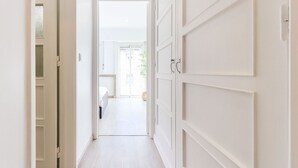 A hallway with white doors and a view into a room with a bed and a window. - Almirante Balcony By Homing (Lisbon)