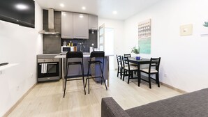 A compact kitchen with modern appliances, a dining area with chairs, and a flat-screen TV mounted on the wall. - Almirante Balcony By Homing (Lisbon)
