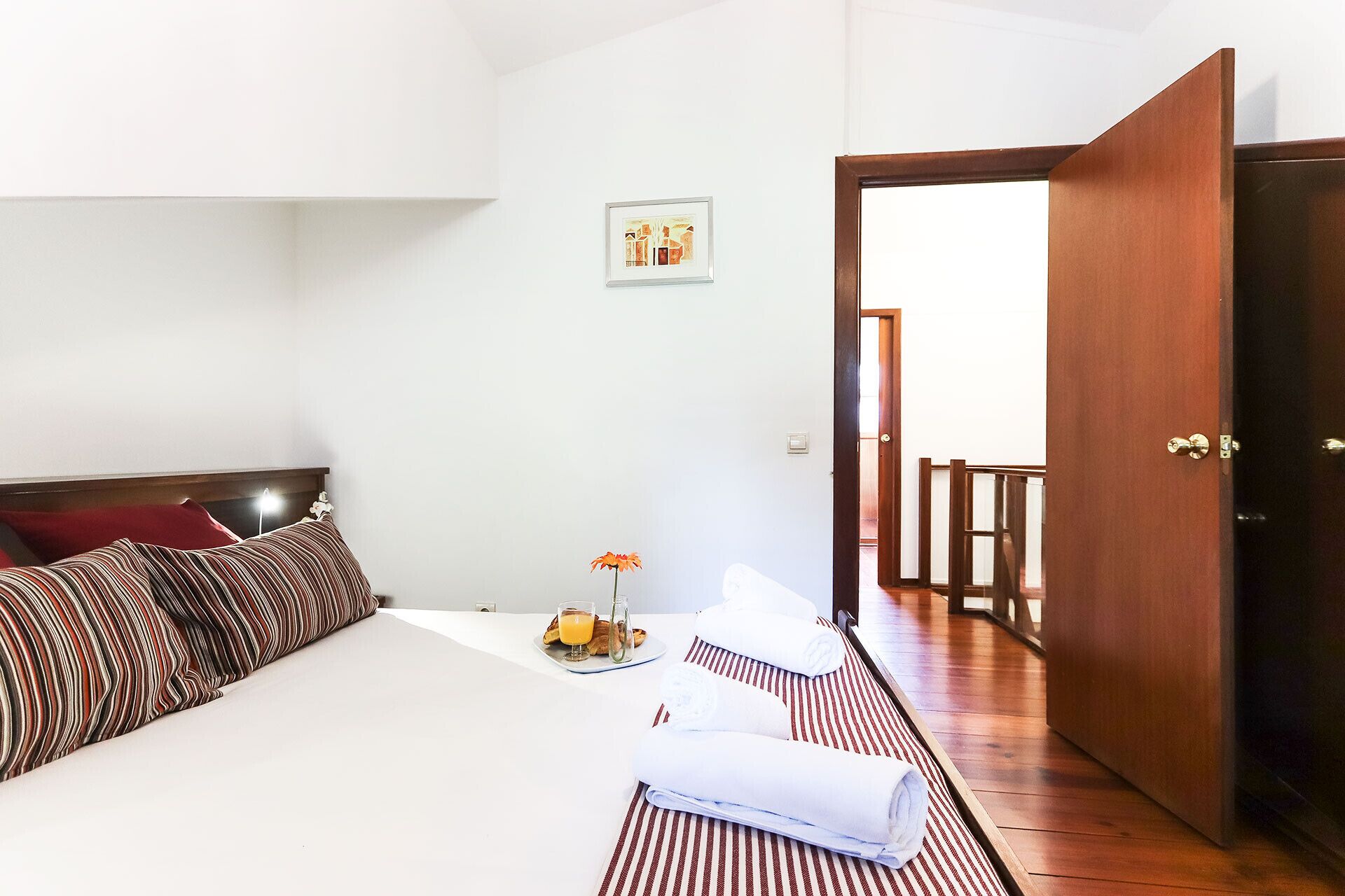 Une chambre d’hôtel avec un lit, des oreillers, une petite table sur laquelle se trouve un verre de jus d’orange, une bouteille et une fleur.