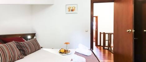 Une chambre d’hôtel avec un lit, des oreillers, une petite table sur laquelle se trouve un verre de jus d’orange, une bouteille et une fleur.
