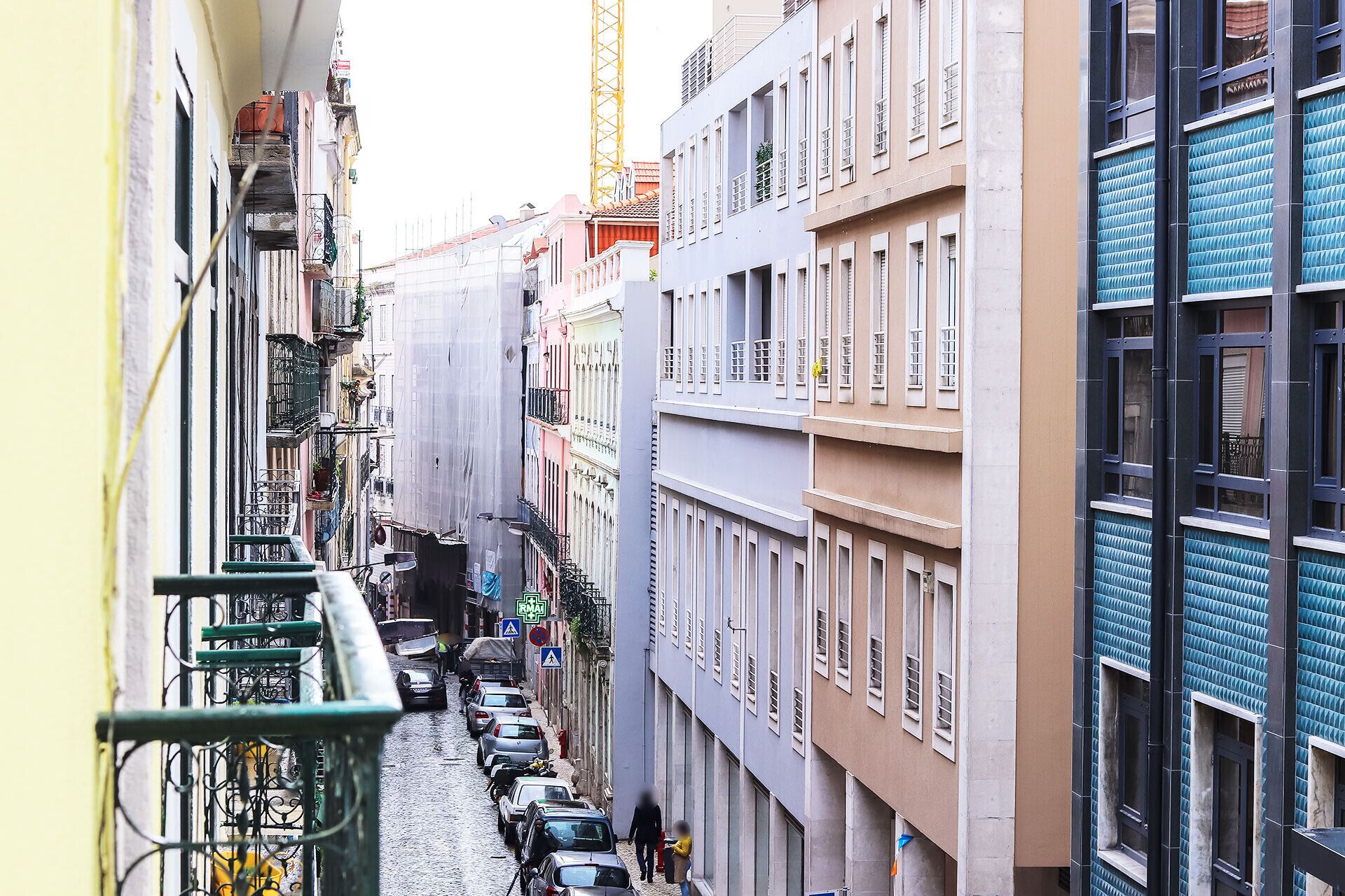 A narrow street lined with multi-story buildings, some with balconies and others with ground-level shops.