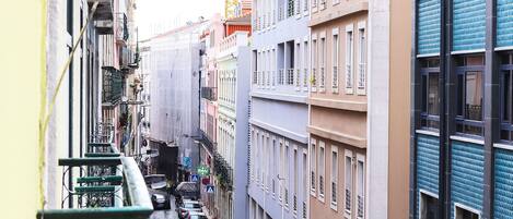 A narrow street lined with multi-story buildings, some with balconies and others with ground-level shops.