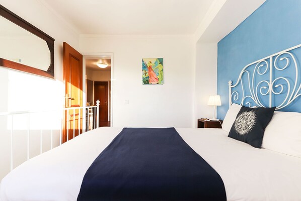 Habitación de hotel con una cama grande, un muro azul decorativo, un cabecero adornado, un cuadro en la pared y vista al pasillo.