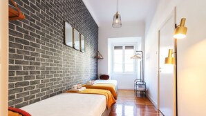 A hotel room with a brick wall, two beds, a hanging light fixture, and a window with a view. - Rato Design With Terrace By Homing (Lisbon)