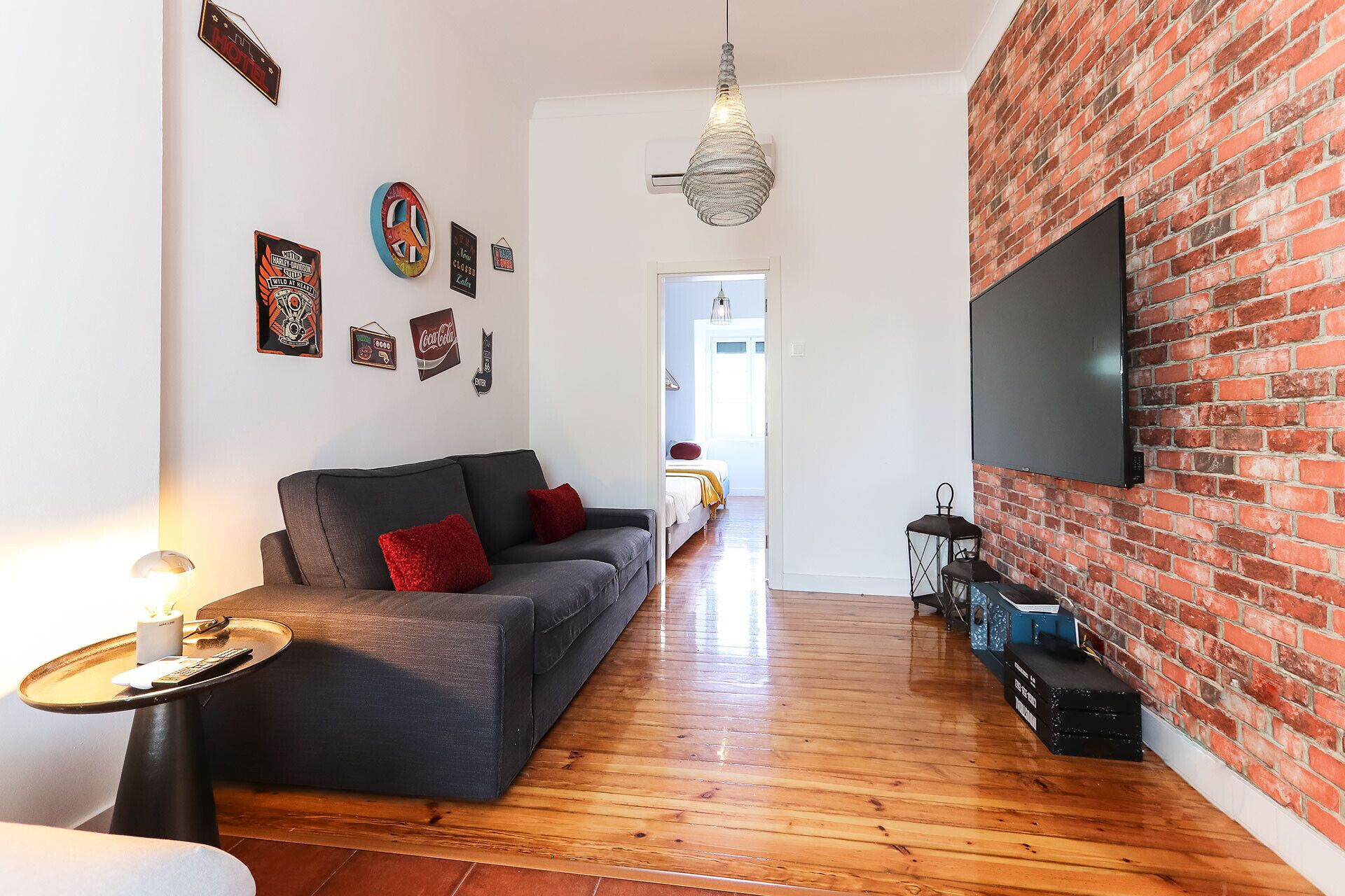 A living room with a sofa, a TV mounted on a brick wall, and various wall decorations.