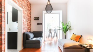 A modern living space with a brick wall, a sofa, a dining area with chairs, and a hanging light fixture. - Rato Design With Terrace By Homing (Lisbon)