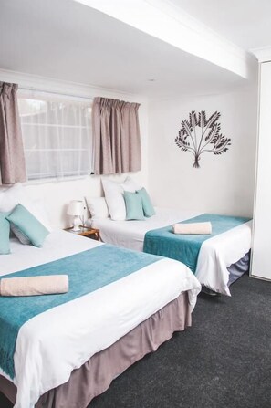 A hotel room with two beds, a window with curtains, a wall decal, and a nightstand with a lamp. - Ferndale Lodge (Randburg)