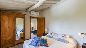 Un dormitorio con un amplio armario de madera, una cama con almohadas estampadas y un techo con vigas a la vista.