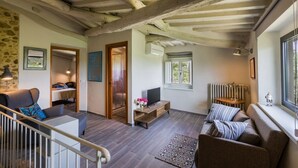 Una sala de estar acogedora con pared de piedra, vigas de madera, un sofá, un televisor y una ventana con vistas.