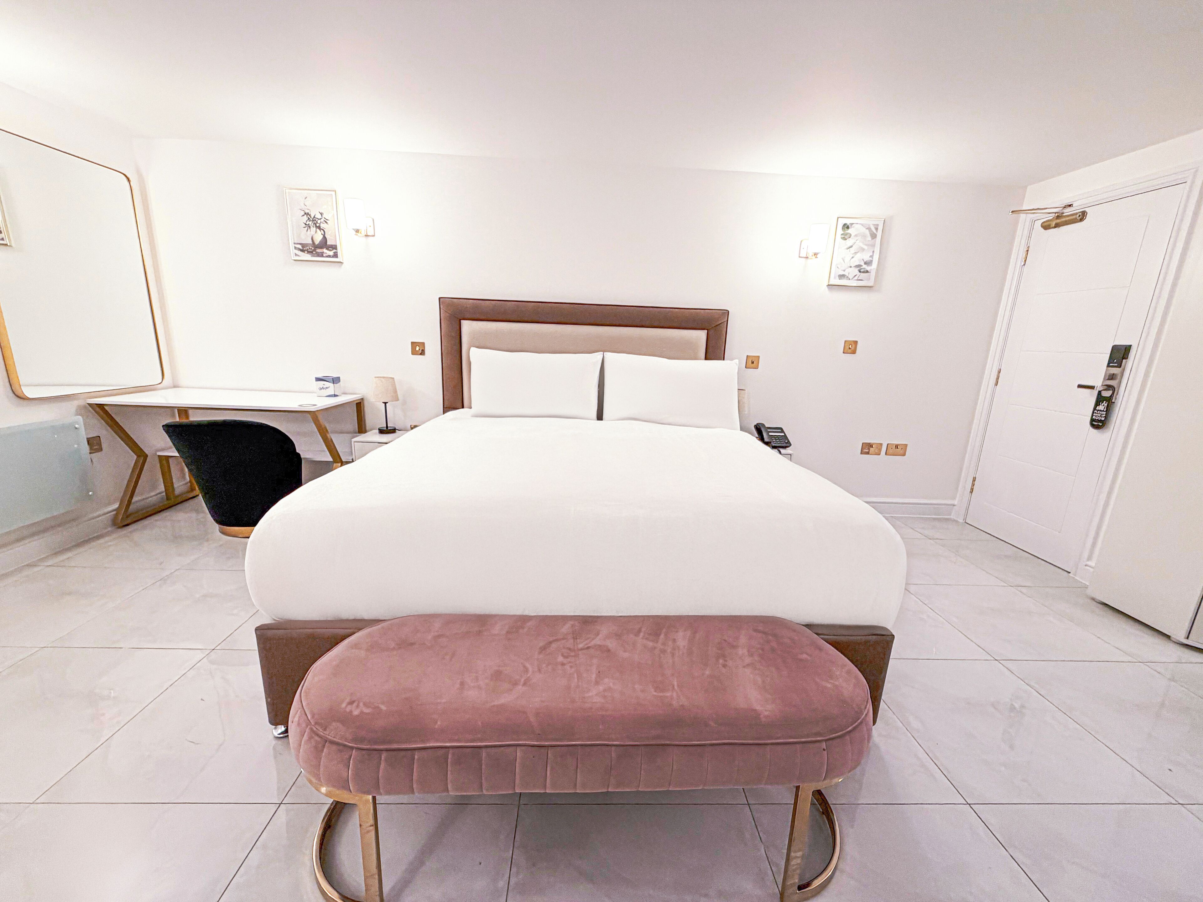 A hotel room with a large bed, a bedside table, a chair, a desk, and a wardrobe.