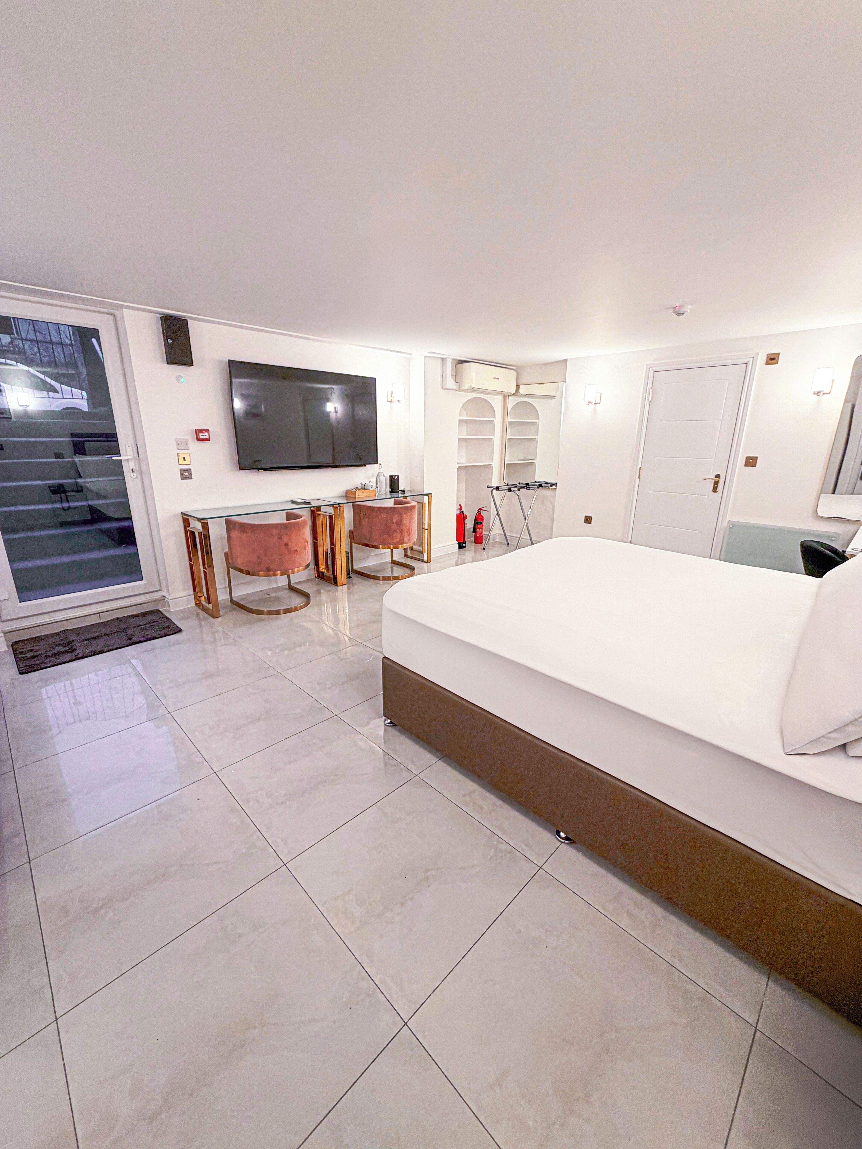 A modern hotel room with a large bed, a desk with a chair, a television, and a view of the outside.