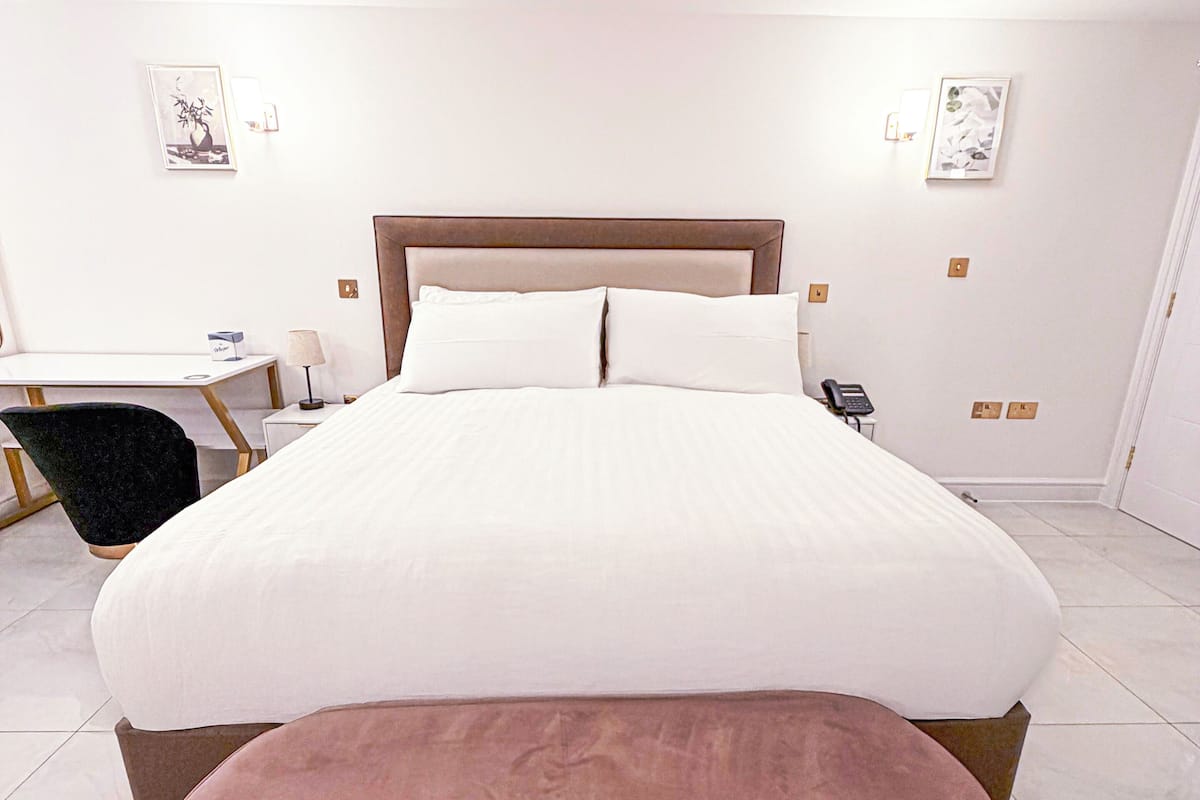 A neatly arranged bedroom with a large bed, a bedside table, a chair, and a desk.