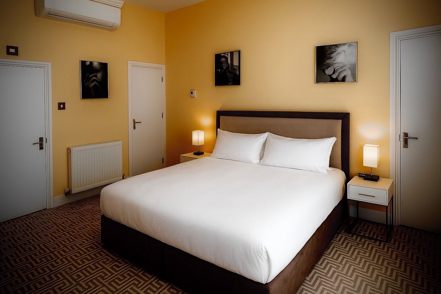 A neatly arranged hotel room with a large bed, two bedside tables with lamps, a radiator, and a patterned carpet.