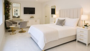 A modern bedroom with a large bed, bedside tables with lamps, a TV, and a seating area with chairs and a small table. - The Hadley Hotel (Barnet)