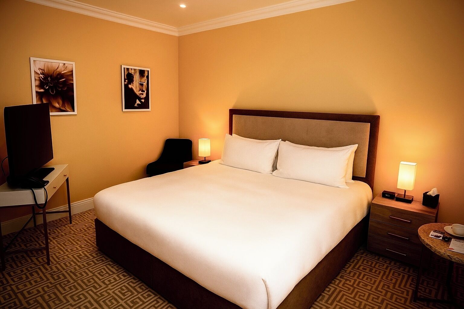A hotel room with a large bed, two bedside tables with lamps, a desk with a chair, and a television.