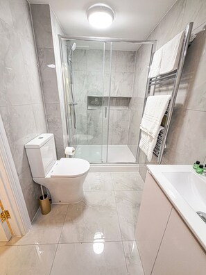 A modern bathroom with a glass-enclosed shower, a toilet, and a bathtub. - The Hadley Hotel (Barnet)