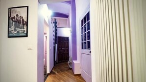 A narrow hallway with wooden flooring, a poster on the wall, and a door with vertical blinds. - Splendida Dimora Negri (Genoa)