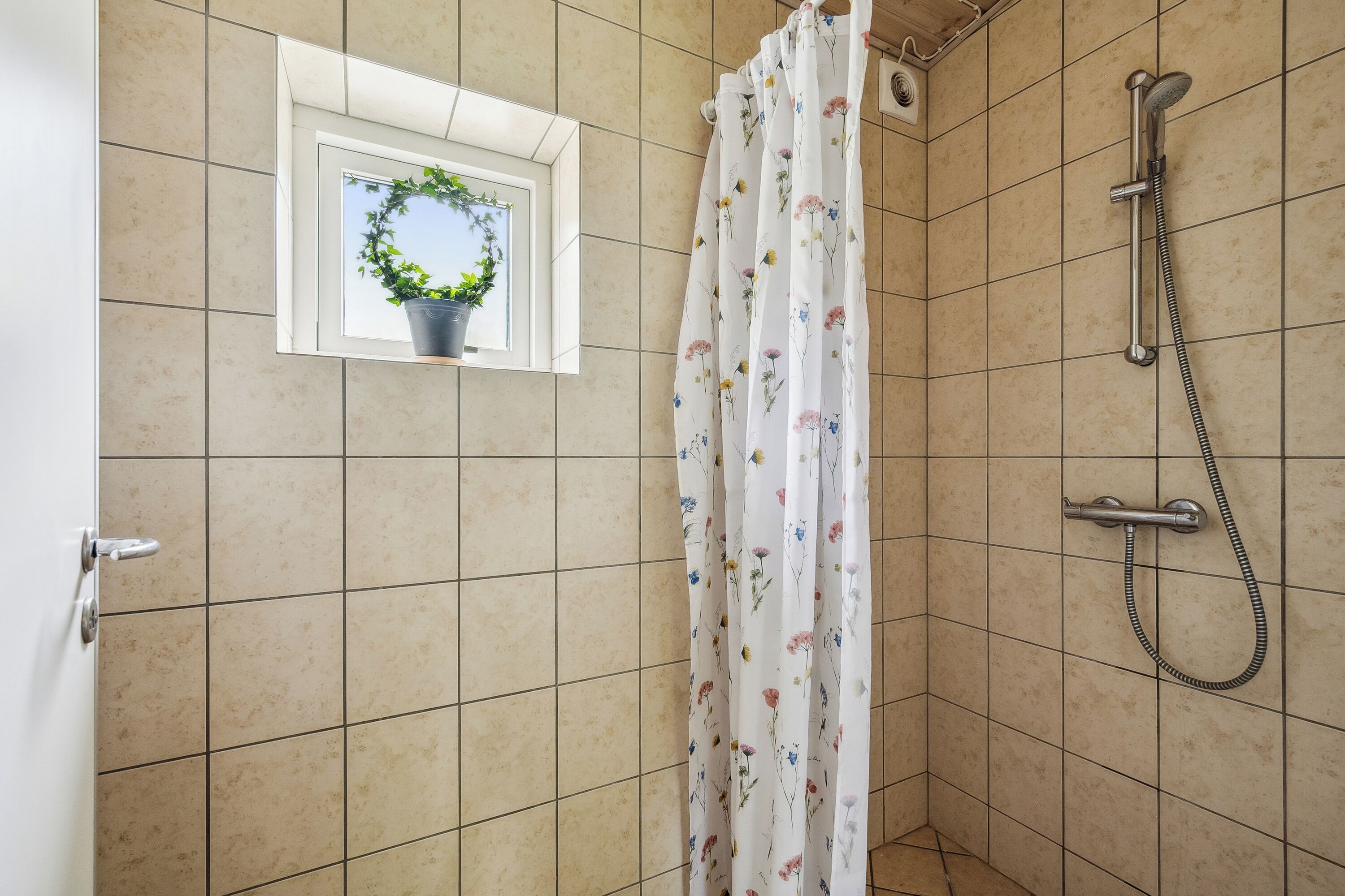 A shower area with a showerhead, curtain, and a window with a plant.