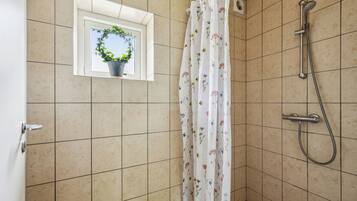 A shower area with a showerhead, curtain, and a window with a plant.