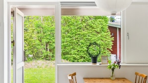 A room with a wooden table, two chairs, a white bed, a large window with a view of greenery, and a hanging light fixture. - Danhostel Stevns (Store Heddinge)