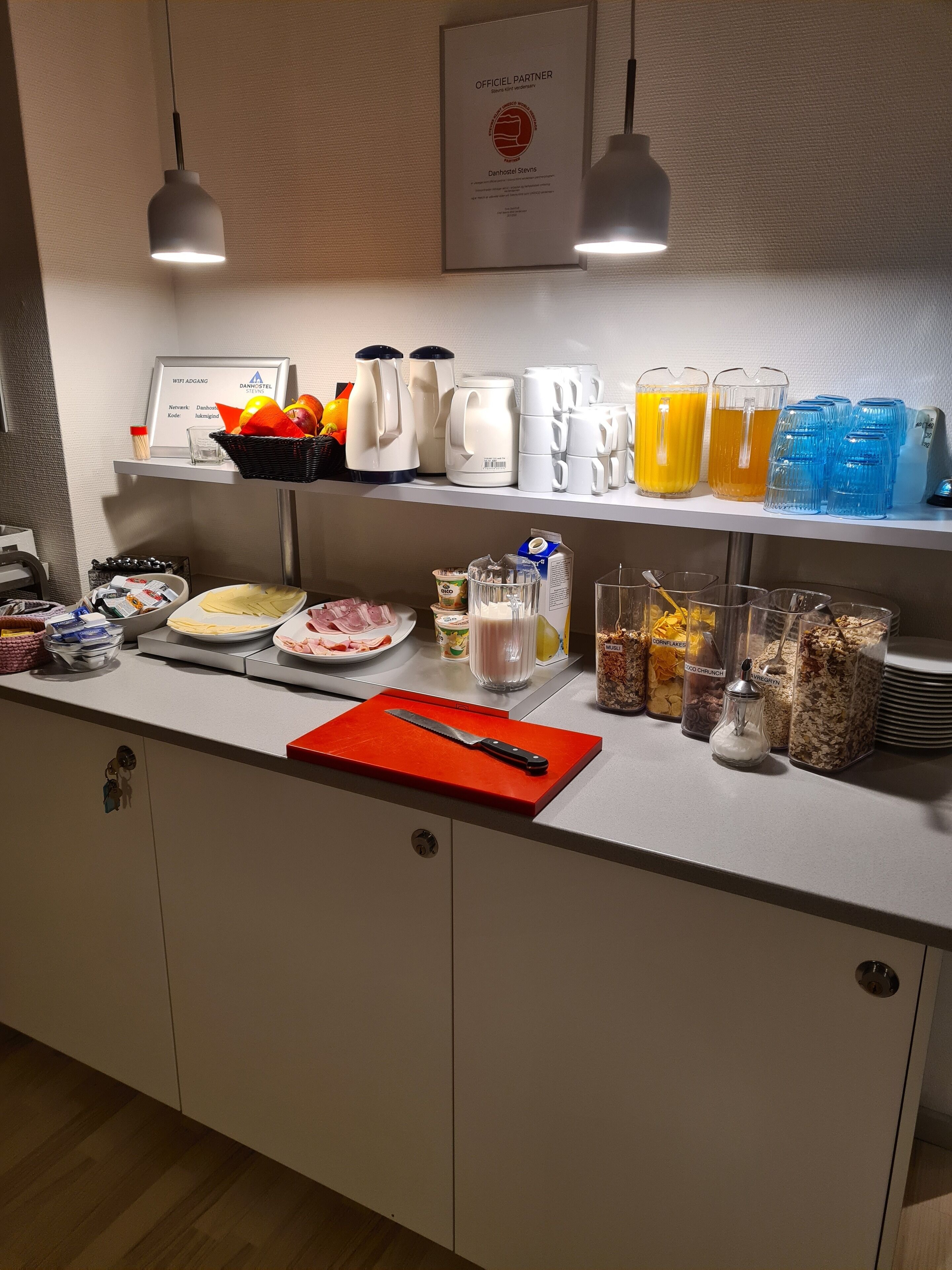 Montaje de un bufé de desayuno con diversas opciones de comida, cafeteras y un cartel que indica la disponibilidad de WiFi.