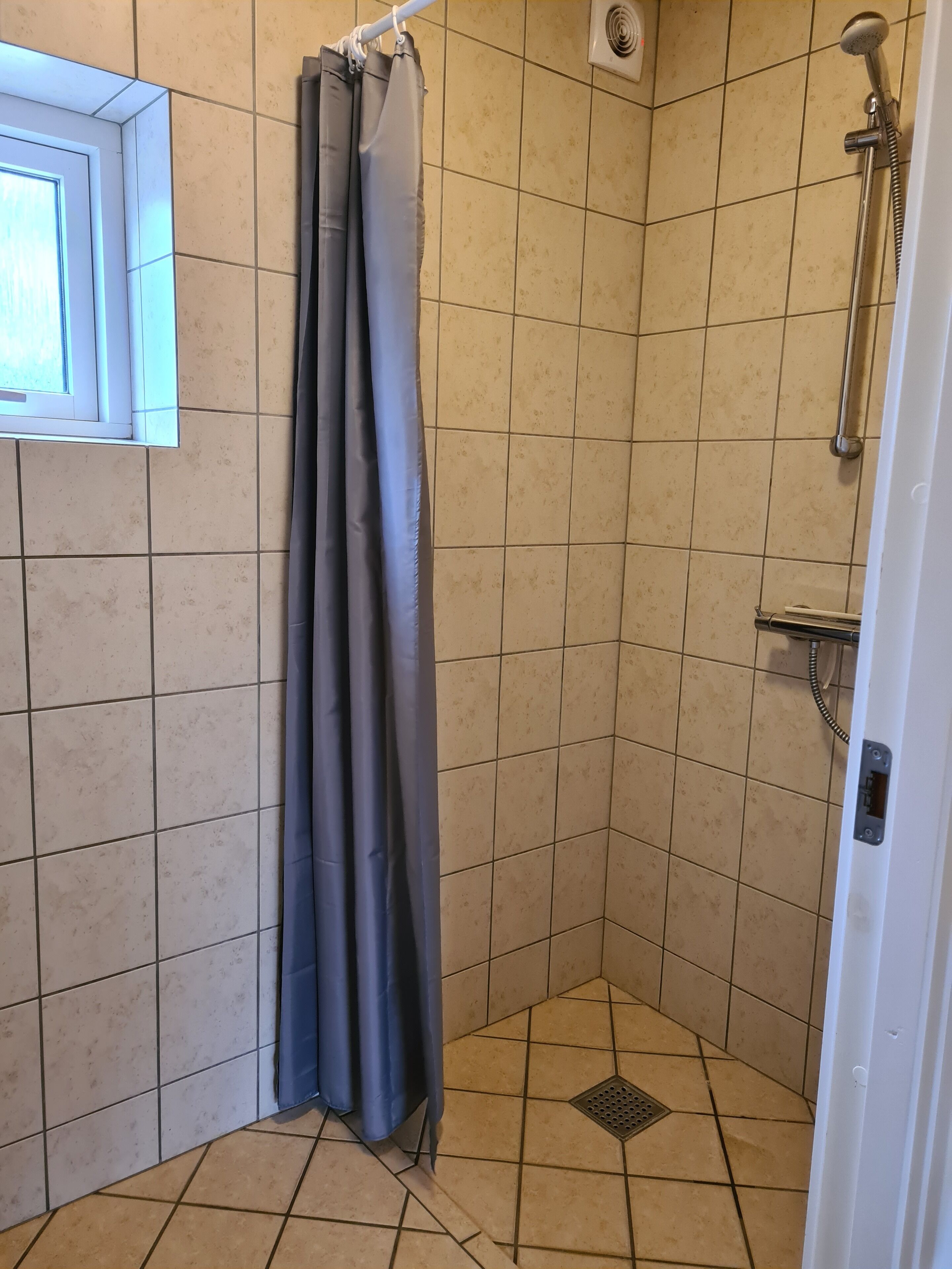 Ein kleiner Duschbereich mit Fliesen, einer Duschbrause, einem Vorhang und einem Fenster.