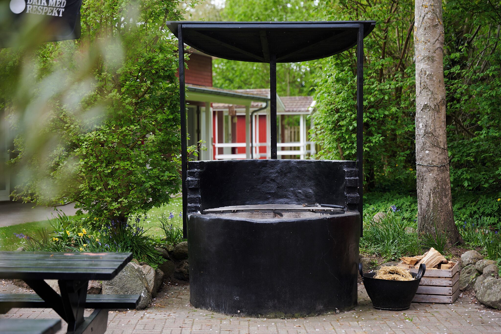 A gazebo with a bench, surrounded by greenery and a brick pathway.