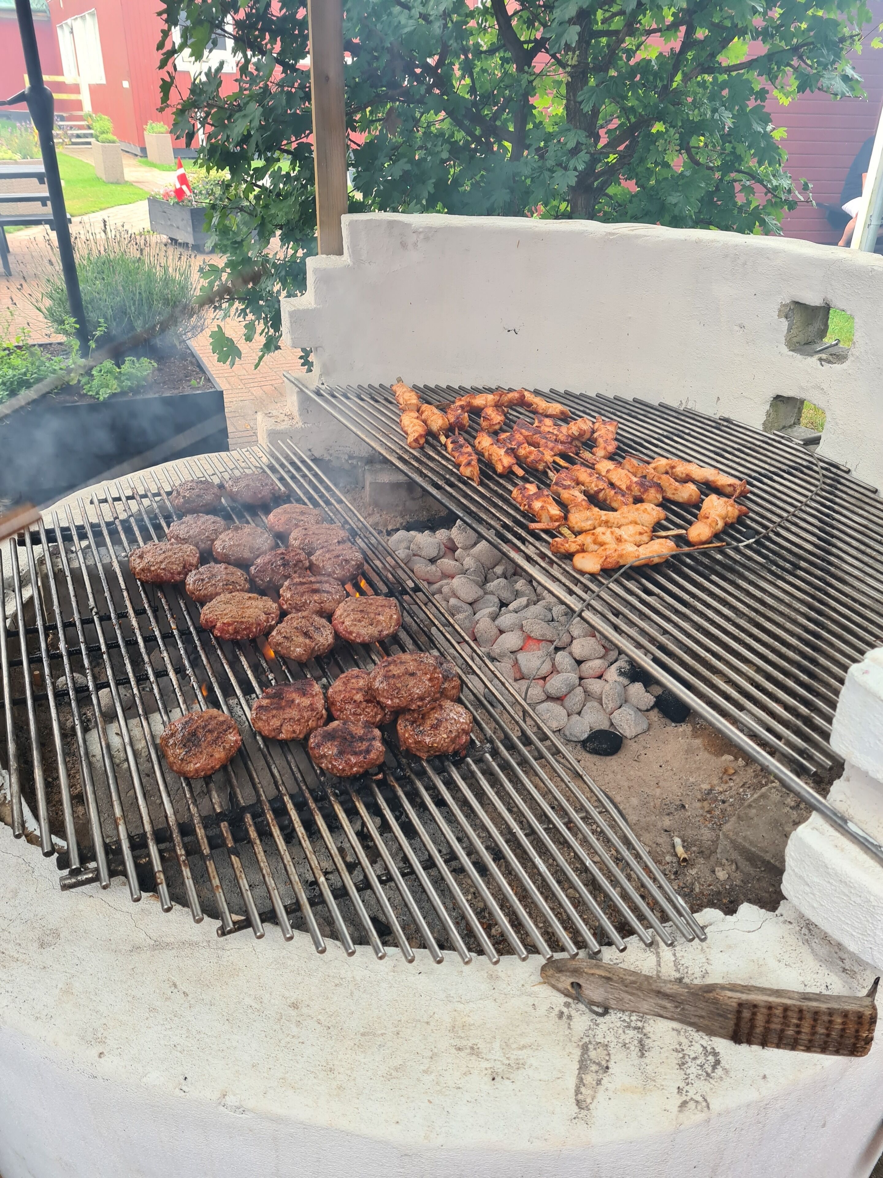 Una parrilla con hamburguesas y brochetas de pollo asándose.