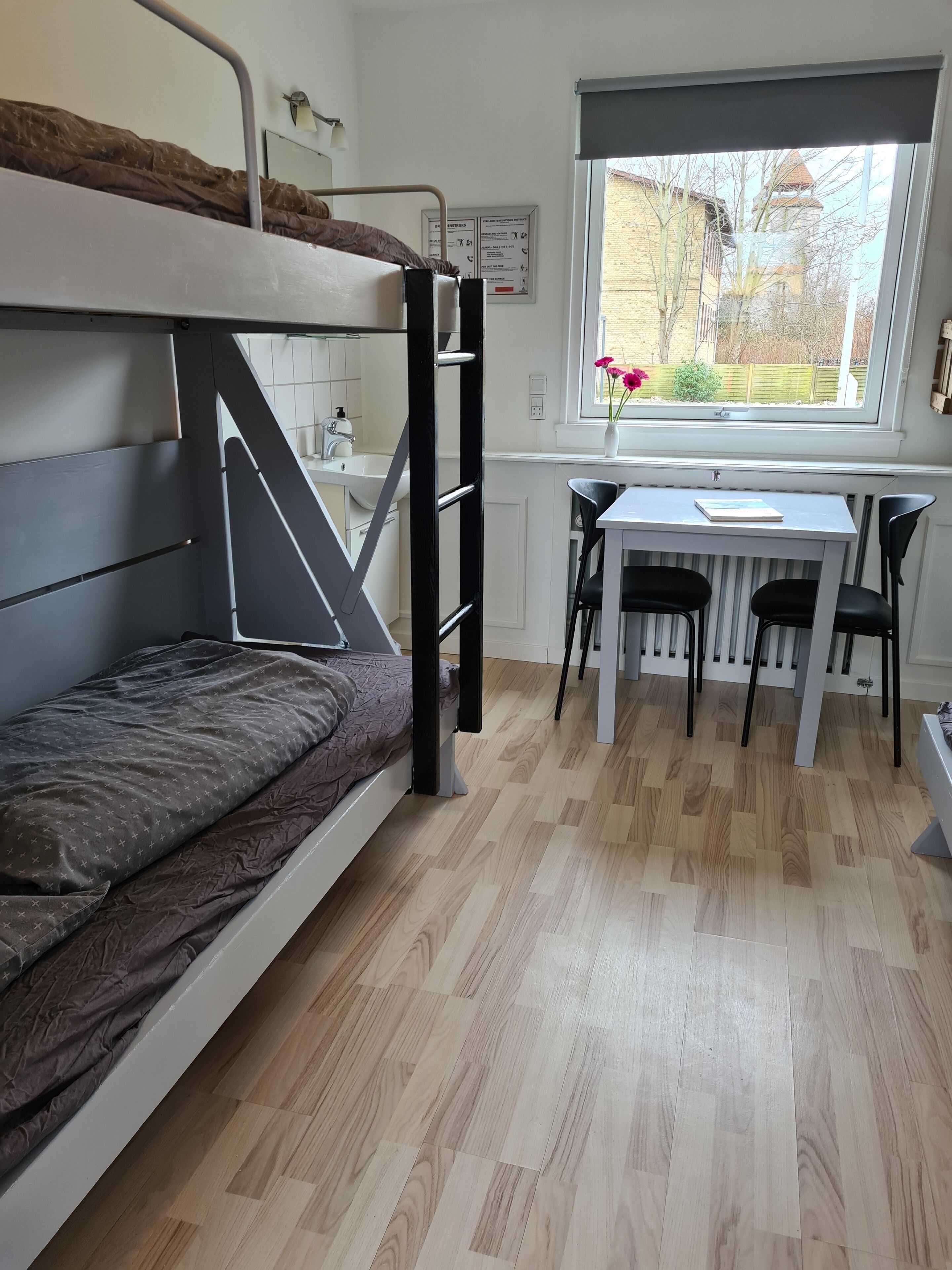 Een stapelbed met bureau en stoelen in een kamer met een raam.