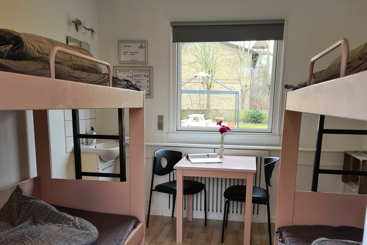 Ett studentrum med våningssängar, ett skrivbord, stolar, ett fönster med utsikt och ett element.