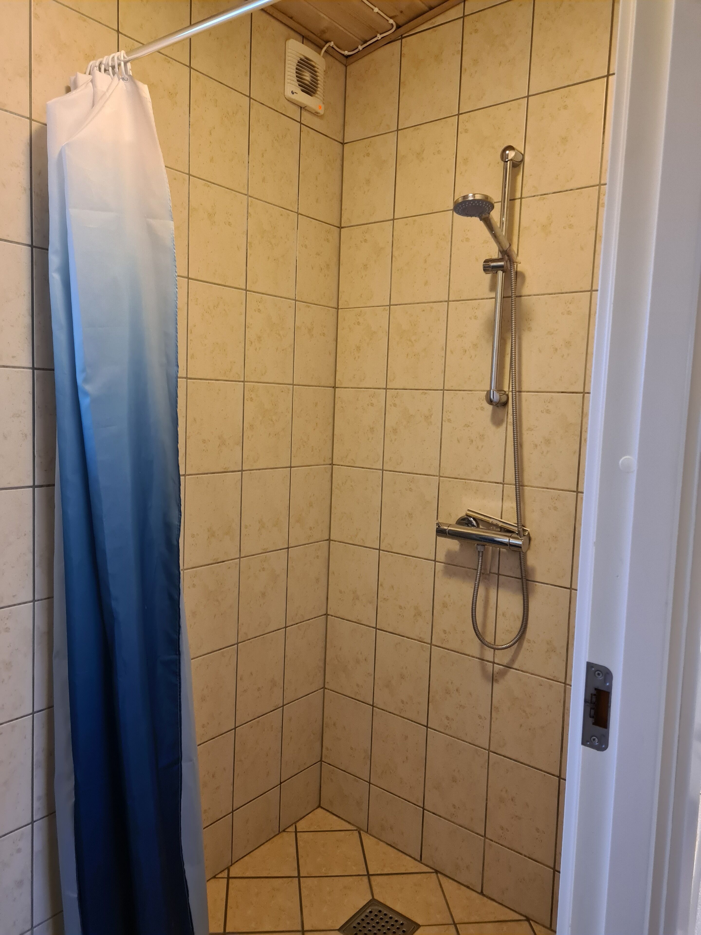 A small, tiled shower room with a showerhead and handheld shower attachment.